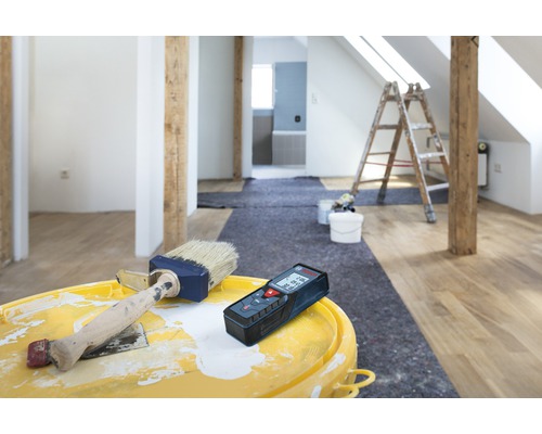 Rénovation d'une pièce avec télémètre laser, peinture et pinceau sur un seau