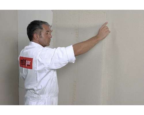 Ein Mann bringt an einer Wand eine Dämmplatte an