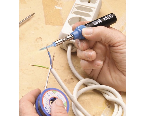 Une main soude une ligne électrique avec un fer à souder. Une bobine d''étain à souder et une multiprise sont posées sur la table.