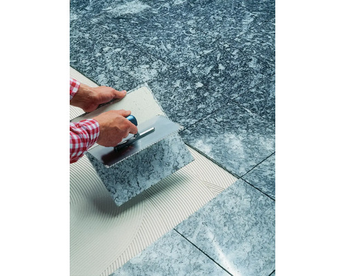 Pose de carreaux de sol gris avec spatule et colle à carrelage