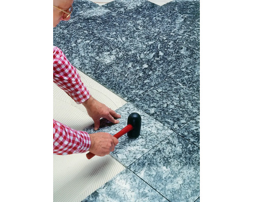 Un homme pose des carreaux de grès cérame à l''aide d''un maillet en caoutchouc