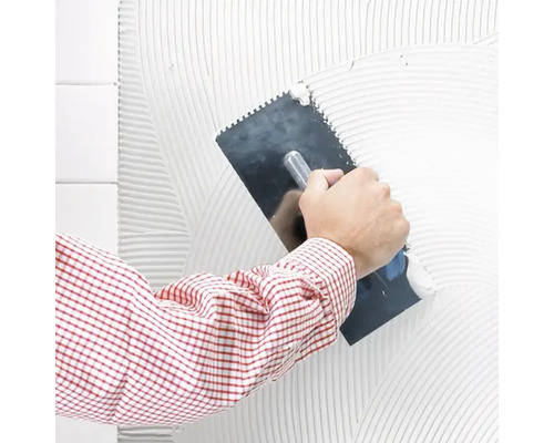 Un homme applique de la colle à carrelage sur un mur avec une spatule crantée.