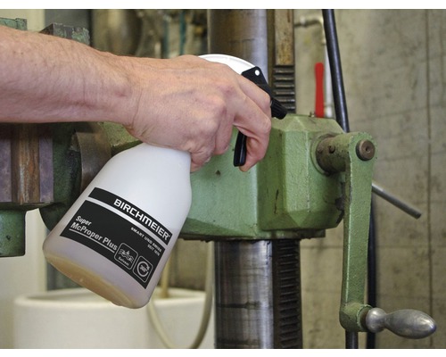 Eine Person sprüht Reiniger auf eine Bohrmaschine.