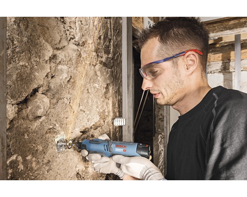 Un homme travaille avec un outil multifonction sur un mur de pierre