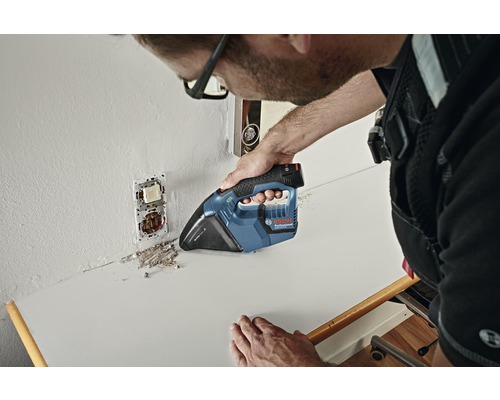 Un artisan aspire la poussière de construction sur un plan de travail à l''aide d''un aspirateur à main sans fil.