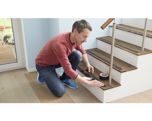 Un homme pose une bande antidérapante sur un escalier en bois. Rouleau de bande antidérapante visible.