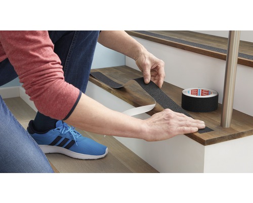 Une personne fixe une bande antidérapante sur une marche d''escalier pour plus de sécurité.