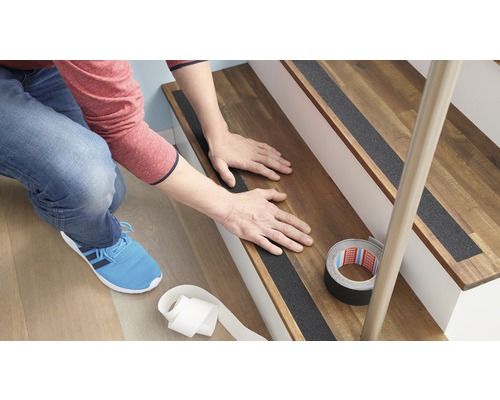 Eine Person bringt Antirutschstreifen auf einer Holztreppe an, um die Sicherheit zu erhöhen.