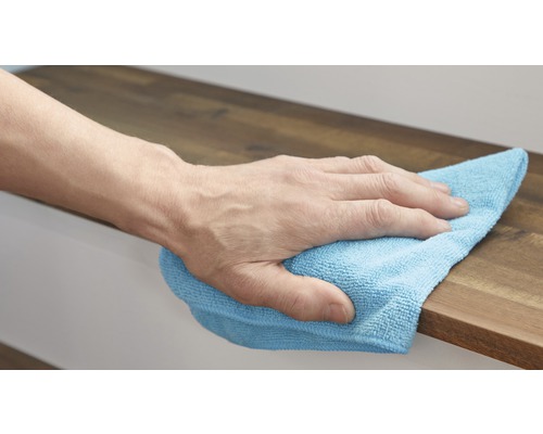 Une main essuie une surface en bois avec un chiffon de nettoyage.