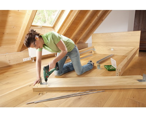 Une personne assemble un lit en bois avec une visseuse sans fil.