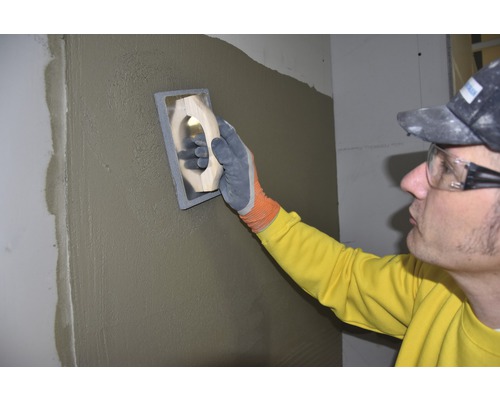 Artisan lissant un mur avec une lisseuse et du plâtre.