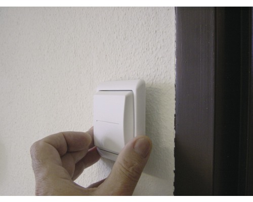 Eine Bedienperson drückt einen Lichtschalter an einer Wand.