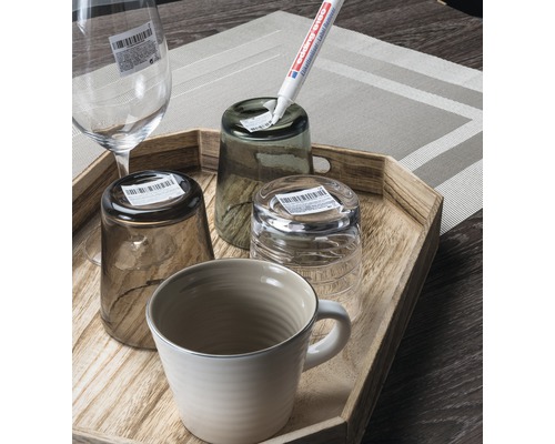 Divers verres et une tasse sont posés sur un plateau en bois. Un stylo pour enlever les étiquettes est utilisé.