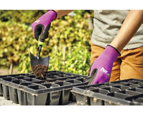 Une personne remplit un plateau de culture avec de la terre et une pelle de jardin, protégée par des gants de jardinage