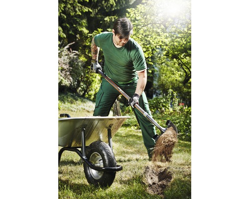 Mann gräbt mit Spaten in einem Garten neben einer Schubkarre.