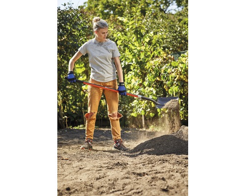 Une femme pelle de la terre avec une bêche dans un jardin.