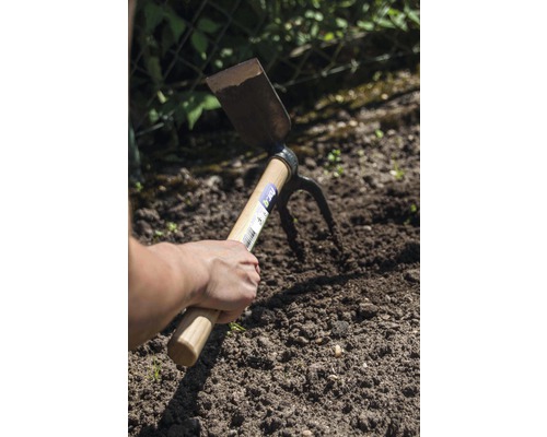 Une main tient une houe double fonction dans la terre du jardin