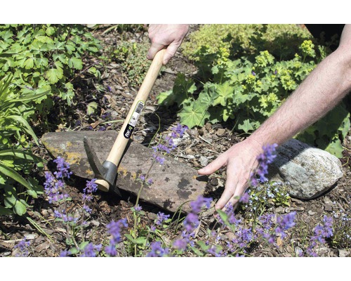 Une personne travaille dans le jardin avec une pioche à manche en bois.