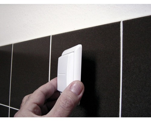 Ein Kippschalter wird vor dunklen Fliesen montiert.