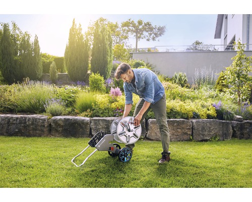 Mann wickelt Gartenschlauch auf Schlauchwagen im Garten auf