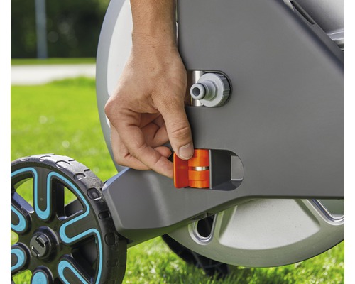 Detailaufnahme einer Hand, die eine orangefarbene Arretierung an einem Gartenschlauchwagen betätigt.