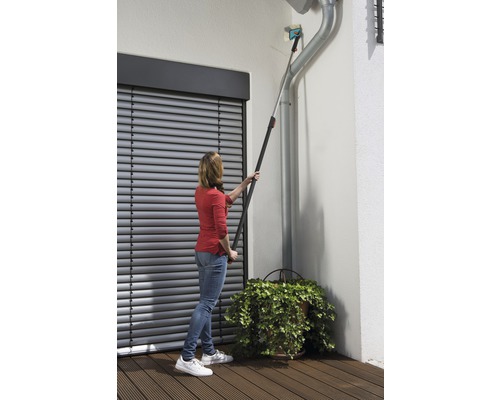 Frau reinigt Dachrinne mit Teleskopstiel-Werkzeug vor Rollladen