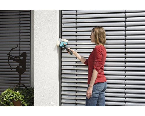 Frau reinigt Jalousien mit einer Jalousiebürste an einem Gebäude