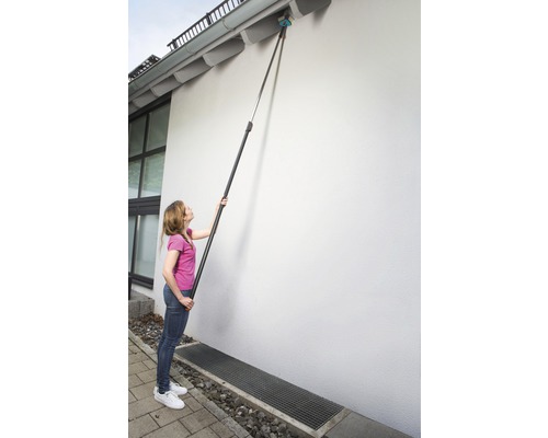 Frau reinigt Dachrinne mit Teleskopstiel und Bürste.