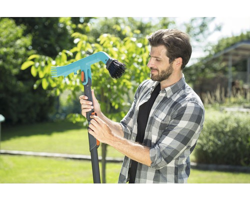 Mann betrachtet eine teleskopierbare Gartenbürste mit Wasseranschluss im Garten.