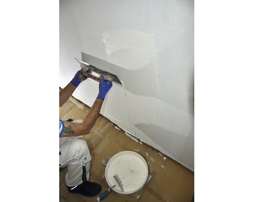 Une personne lisse un mur avec une taloche et de l''enduit.