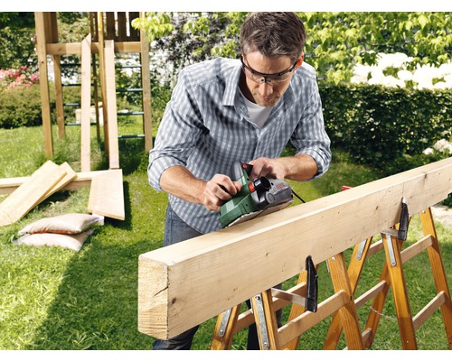 Mann hobelt ein Holzbrett im Freien mit einem Elektrohobel