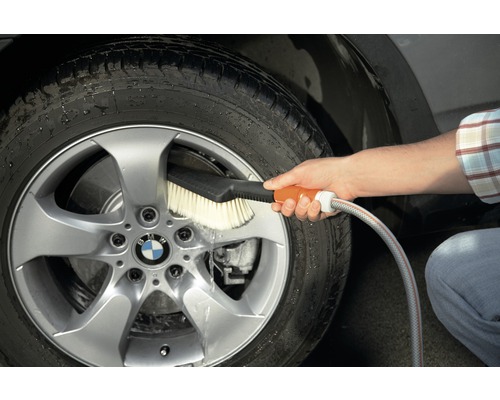 Eine Person reinigt ein Autorad mit einer Waschbürste und einem Wasserschlauch