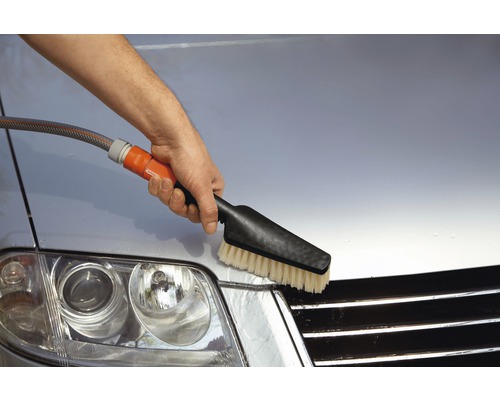 Eine Person reinigt ein Auto mit einer Waschbürste und einem Wasserschlauch.