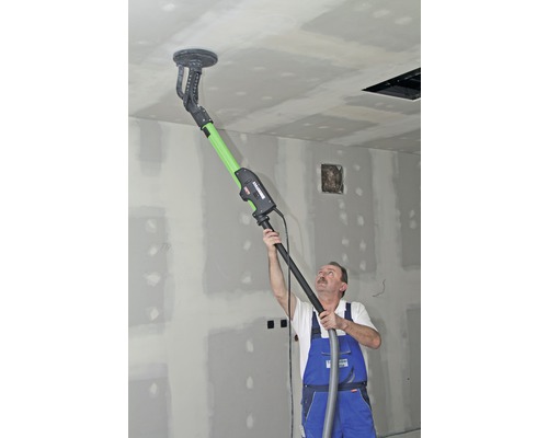 Un homme ponce un plafond avec une ponceuse à long manche dans une pièce.