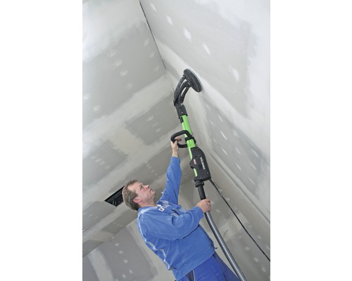 Un homme ponce un mur en plaques de plâtre avec une ponceuse à plaques de plâtre