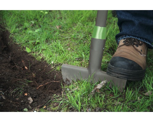 Jardinage avec un coupe-bordures, un pied chaussé sur le coupe-bordures
