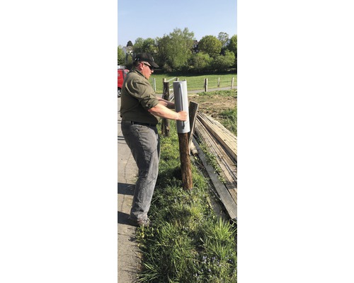 Eine Person befestigt einen Pfostenschuh an einem Zaunpfosten.
