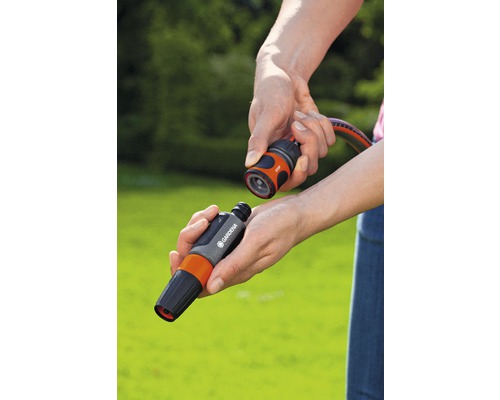 Des mains raccordent un raccord de tuyau Gardena à un connecteur de tuyau