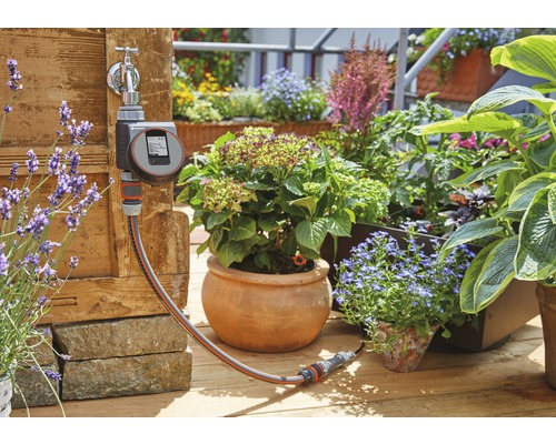Robinet Gardena avec programmateur d''arrosage et tuyau d''arrosage devant un jardin planté
