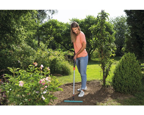 Frau harkt den Boden im Garten mit einem Rechen