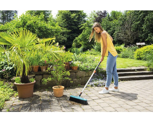 Frau kehrt Steinterrasse mit Strassenbesen in einem Garten