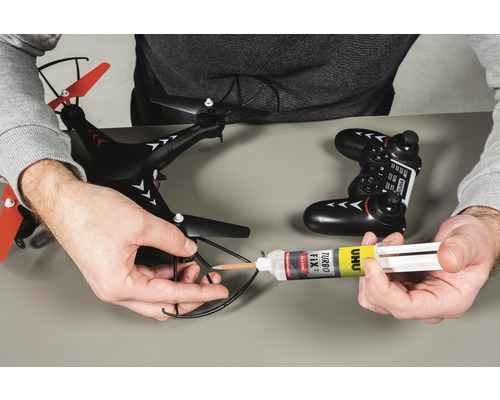 Eine Drohne wird mit Klebstoff repariert. Fernbedienung und Klebstoff sind auch zu sehen.