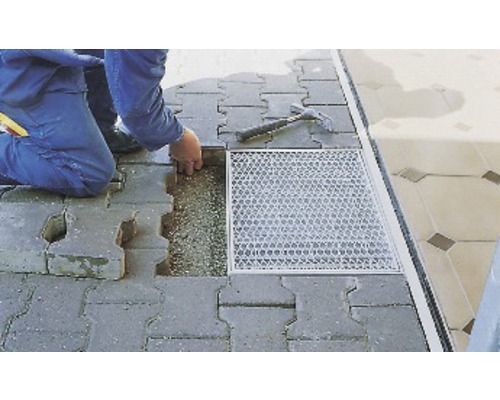 Un homme pose des pavés en béton avec un marteau et une rigole de drainage.
