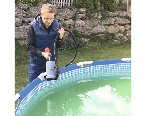 Un homme utilise une pompe de piscine au bord d''une piscine dans le jardin.
