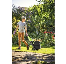 Frau zieht einen Gartenwagen voller Laub durch den Garten.