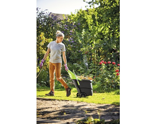Frau zieht einen Gartenwagen voller Laub durch den Garten.