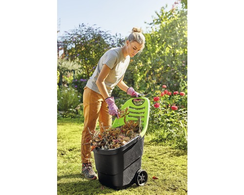 Frau befüllt einen Gartenwagen mit Gartenabfällen im Garten.
