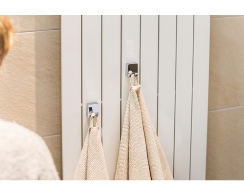 Radiateur blanc avec deux serviettes et crochets chromés dans la salle de bains.