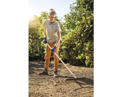 Une femme ratisse la terre dans le jardin avec un râteau.