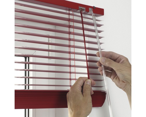 Nahaufnahme einer Person, die eine rote Jalousie mit einer Schnur und einem transparenten Stab bedient.